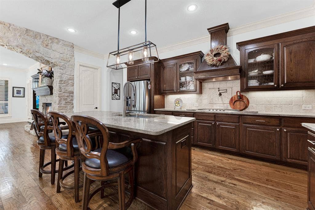 7032 PORTOBELLO Drive, Plano, TX 75024 Polished granite countertops reflect linear pendant lights, surrounded by deep-toned cabinetry and detailed molding. Visualize plating gourmet weekend hors d'oeuvres while guests gather comfortably around the central island.
