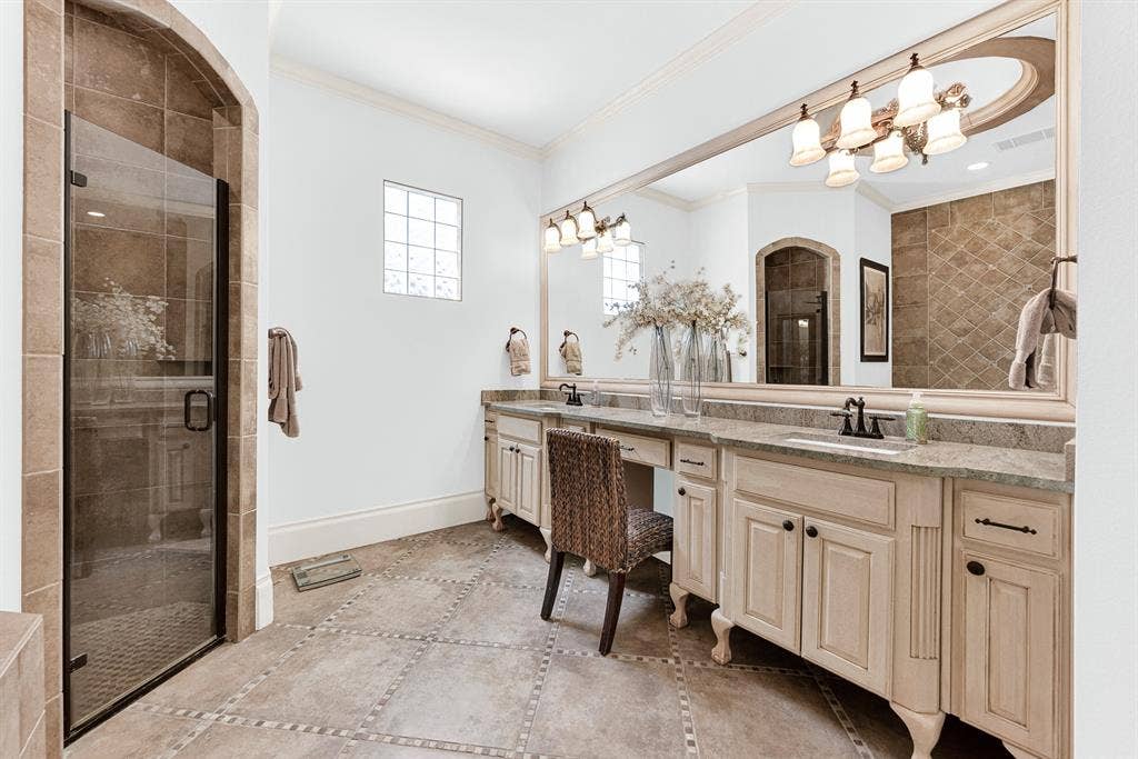 7032 PORTOBELLO Drive, Plano, TX 75024 An expansive double vanity with a seated makeup station stretches beneath a wall-mounted glass mirror. Complete your morning skincare routine with plenty of room to stretch out and organize.