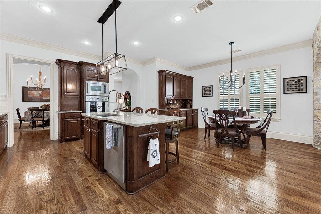 7032 PORTOBELLO Drive, Plano, TX 75024 Shuttered windows flood the casual dining space with gentle sunlight beside a custom built-in beverage station. Enjoy relaxing Sunday morning breakfasts bathed in natural light before starting your day. Built-in stainless steel appliances blend into rich wood cabinetry under glowing task lighting. Imagine prepping a favorite family recipe with every essential tool conveniently within arm’s reach.