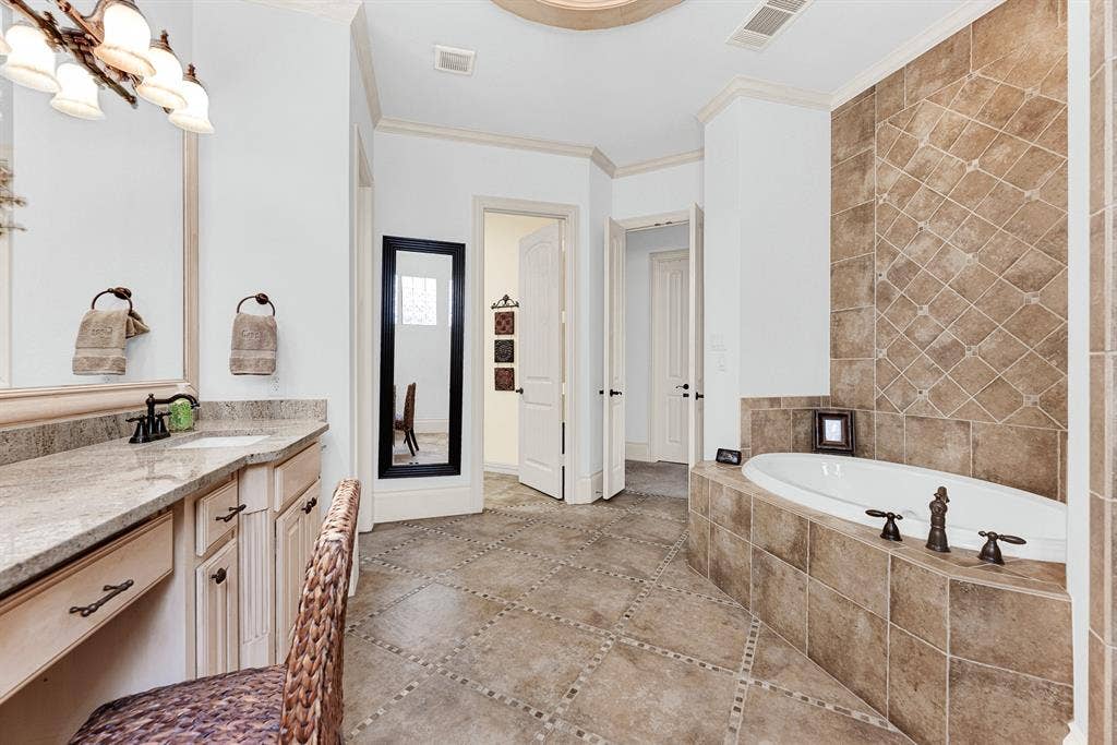 7032 PORTOBELLO Drive, Plano, TX 75024 A private doorway connects the en-suite directly to the laundry room for ultimate daily efficiency. Enjoy the effortless convenience of streamlining laundry tasks right steps from your closet. Earth-toned tile extends floor-to-ceiling behind the deep jetted soaking tub, adding rich texture to the quiet corner. Indulge in an extended evening soak surrounded by calm, neutral finishes.