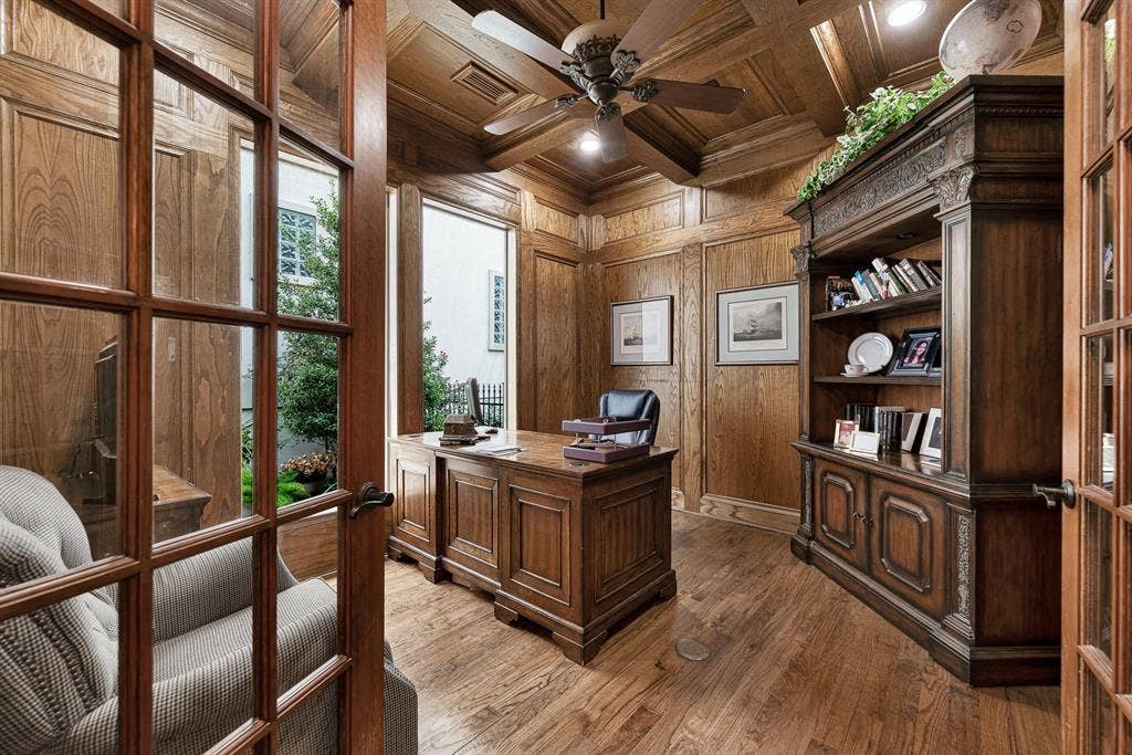 7032 PORTOBELLO Drive, Plano, TX 75024 Rich wood wainscoting and a detailed coffered ceiling frame natural daylight streaming through full-height courtyard windows. Settle in for focused morning work while enjoying calming views of lush outdoor greenery