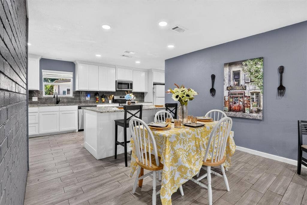 8117 Rush Street, Benbrook, TX 76116 Open-concept kitchen and dining area featuring white cabinetry with stainless steel appliances, wood-finish flooring throughout, and a center island with seating