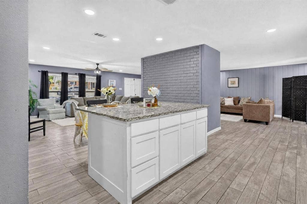 8117 Rush Street, Benbrook, TX 76116 Open-concept kitchen and living area featuring a white cabinetry island with wood-finish countertops, stainless steel appliances, gray subway tile backsplash, recessed ceiling lighting, and wood-finish flooring throughout