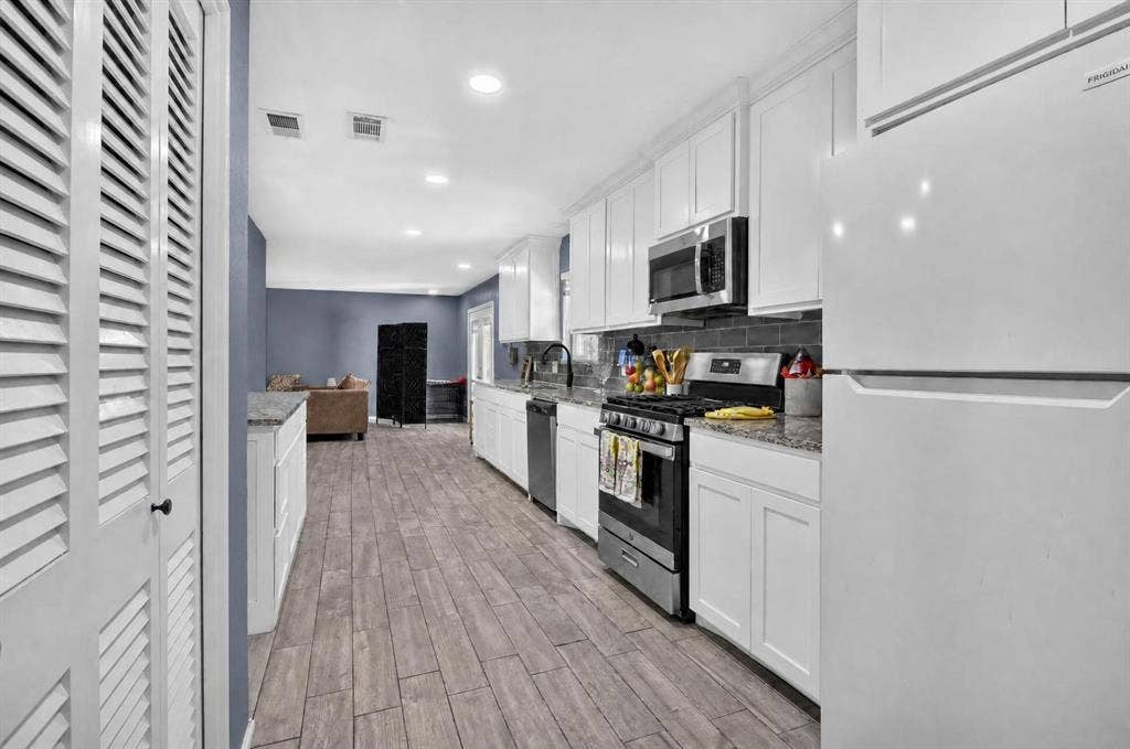 8117 Rush Street, Benbrook, TX 76116 Modern kitchen featuring white cabinetry, stainless steel appliances including a gas range and built-in microwave, quartz countertops, and wood-finish flooring that extends into the adjoining living areas
