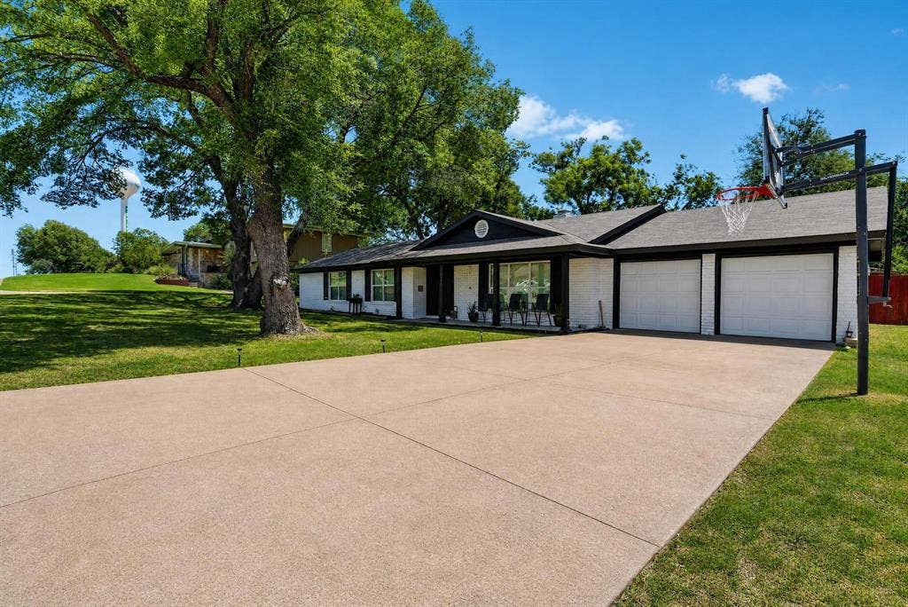 8117 Rush Street, Benbrook, TX 76116 Expansive concrete driveway with triple-car garage featuring overhead doors and black metal framing