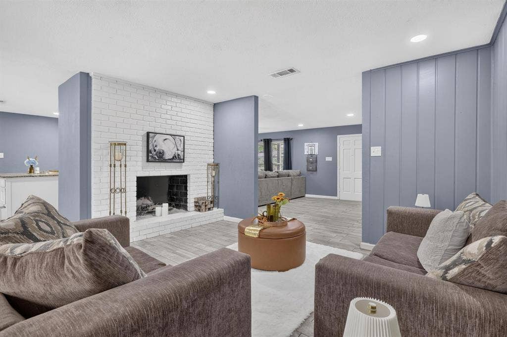 8117 Rush Street, Benbrook, TX 76116 Spacious primary living area featuring a white subway brick fireplace with hearth, light wood-finish flooring, and recessed ceiling lighting