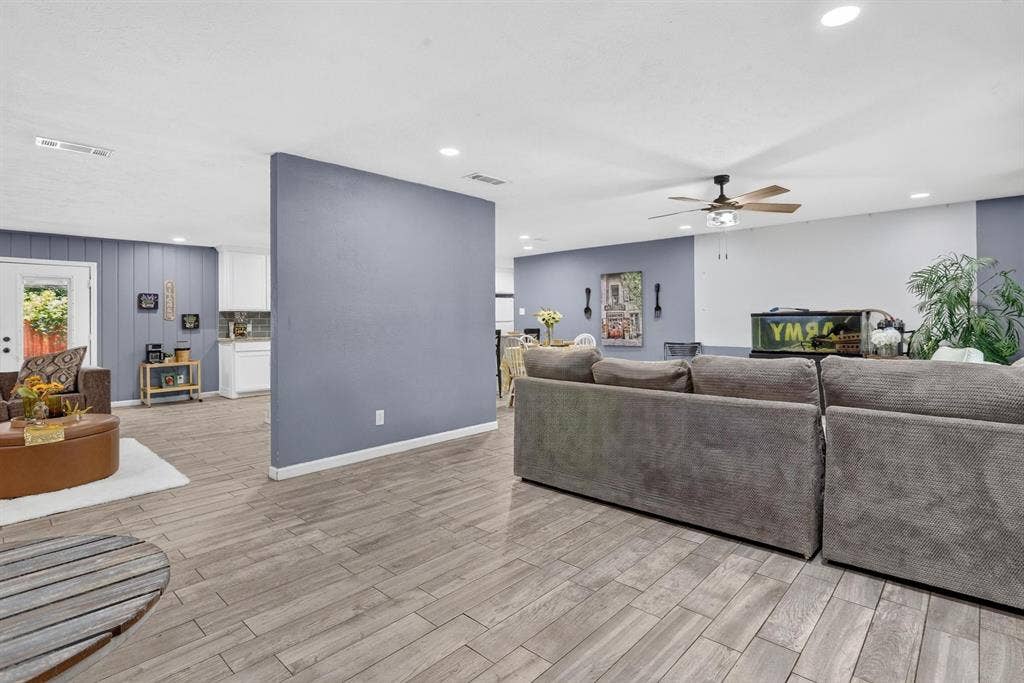 8117 Rush Street, Benbrook, TX 76116 Open-concept living area featuring plank-style wood-finish flooring, a large architectural accent wall in slate blue, recessed ceiling lighting, and a ceiling fan