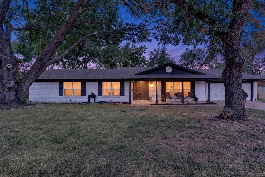 8117 Rush Street, Benbrook, TX 76116 Modern single-story residence with clean-lined architecture, featuring a white exterior with black trim accents and multiple glass doors opening to the rear grounds