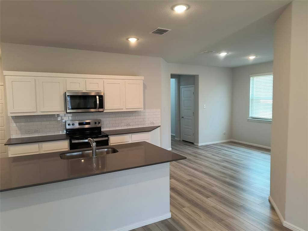 320 Leopold Trail, Greenville, TX 75402 Kitchen featuring white shaker cabinetry, stainless steel appliances, subway tile backsplash, and a large island with an undermount sink