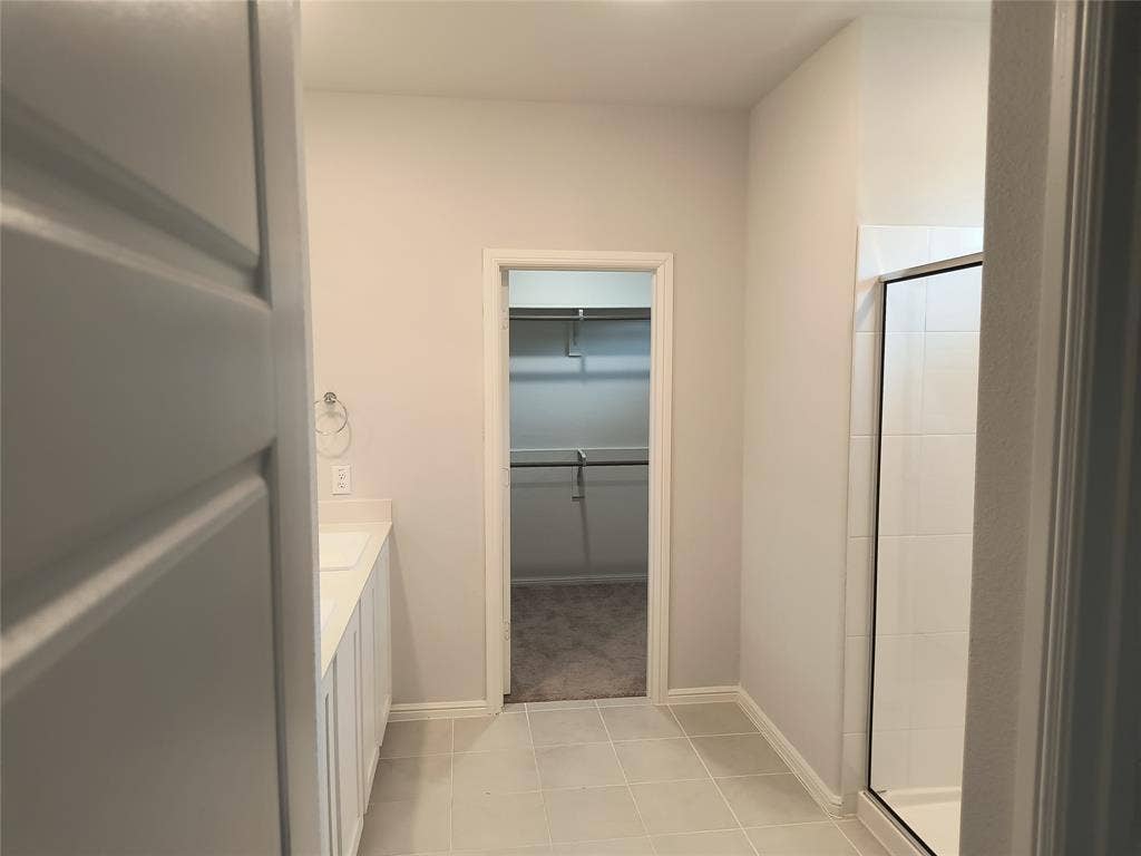 320 Leopold Trail, Greenville, TX 75402 Tile flooring, white vanity with integrated sink, walk-in shower with clear glass enclosure, walk-in closet with built-in shelving and hanging rods