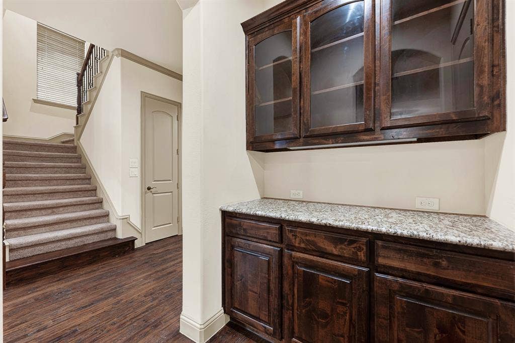 7013 BROOK FOREST Circle, Plano, TX 75024 Glass-front upper cabinetry and dedicated granite serving surfaces tuck neatly beside the walk-in storage access and stairwell. It serves as an ideal staging station for mixing signature cocktails or decanting wine during dinner parties.