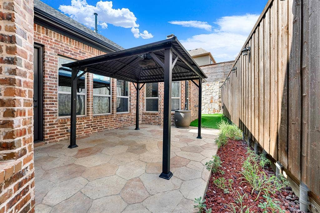 7013 BROOK FOREST Circle, Plano, TX 75024 A stamped concrete courtyard extends beneath a dark metal-roofed pavilion, framed by privacy fencing and warm brick facades. It sets the scene for casual weekend barbecues, grilling burgers while friends gather comfortably in the open breeze.