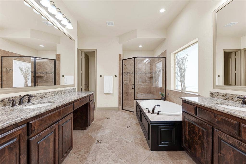 7013 BROOK FOREST Circle, Plano, TX 75024 Dual granite vanities face each other across diagonal ceramic tilework, framing a raised corner glass shower stall. Picture a stress-free weekday morning routine, with plenty of private room for two people getting ready at once.