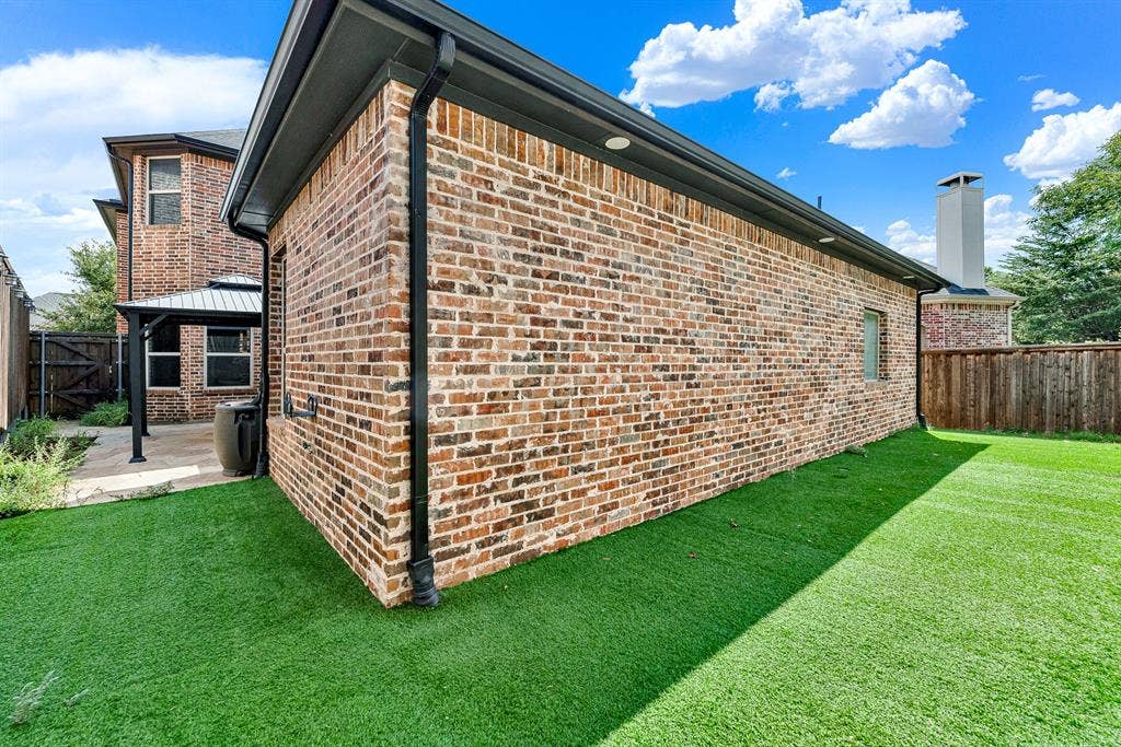 7013 BROOK FOREST Circle, Plano, TX 75024 Vibrant, low-maintenance synthetic turf wraps neatly around the solid brick exterior wall, framed by perimeter cedar fencing. It offers an ideal zero-upkeep green space where pets and kids can play freely without tracking mud inside.