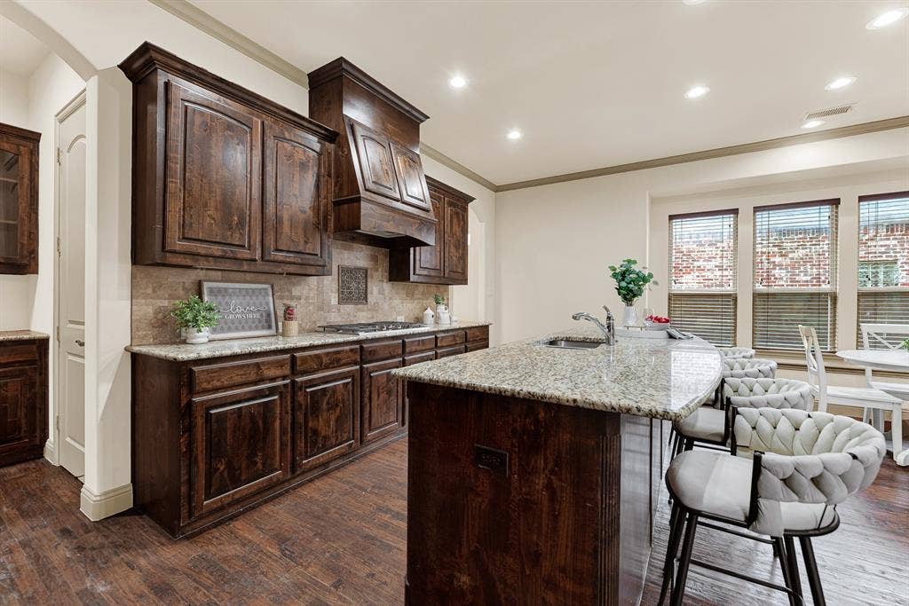7013 BROOK FOREST Circle, Plano, TX 75024 The curved breakfast counter pairs with a textured tile backsplash that catches ambient warmth from nearby side windows. Picture breezy Saturday mornings sharing freshly flipped blueberry pancakes while morning sun brightens the room.