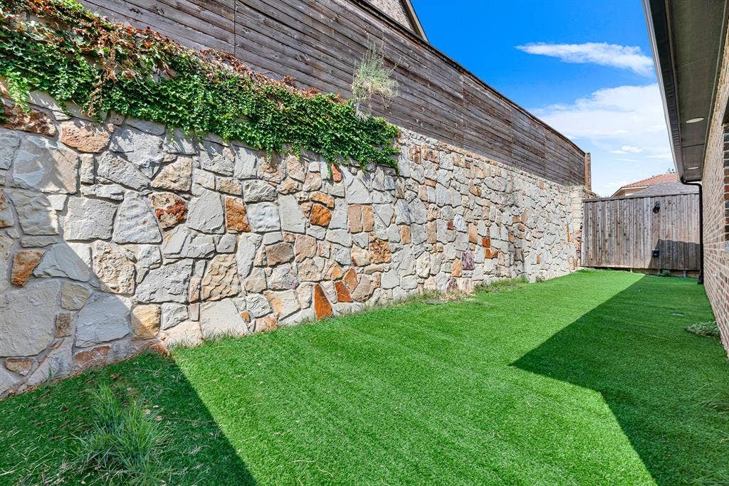 7013 BROOK FOREST Circle, Plano, TX 75024 A towering native stone retaining wall crowned with climbing greenery forms a dramatic, private garden backdrop bathed in afternoon sun. Picture relaxing with a cool drink on warm evenings, enveloped by rustic textures and total backyard seclusion.