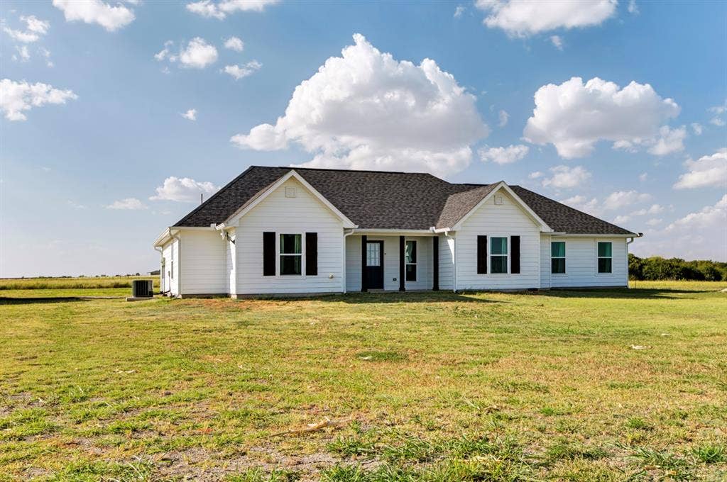 2433 Trlica Road, West, TX 76691 White siding exterior with a dark asphalt shingle roof, black window shutters, and a dark front door