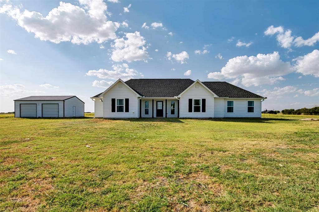 2433 Trlica Road, West, TX 76691 White siding exterior with black shutters, dark shingle roof, and a detached two-car garage