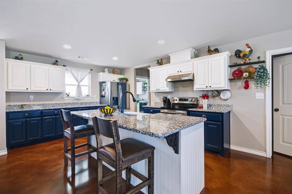 2433 Trlica Road, West, TX 76691 Kitchen featuring two-tone cabinetry with white upper and navy lower cabinets, a central island with a granite-style countertop, stainless steel appliances, and a built-in oven and range
