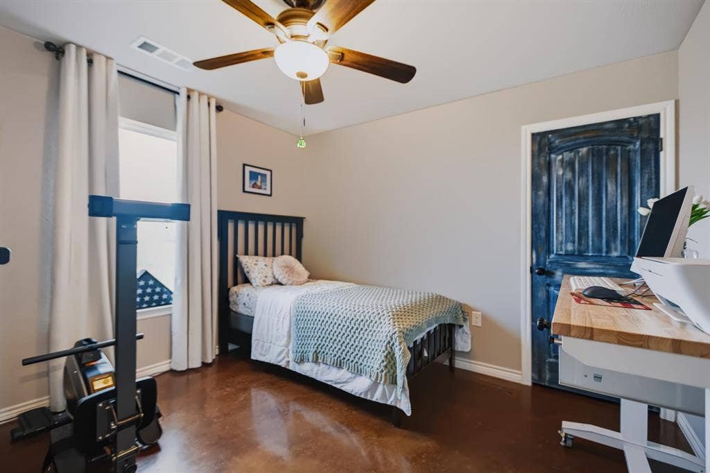 2433 Trlica Road, West, TX 76691 Guest Room 1Wood-finish flooring, ceiling fan with light fixture, window with roller shade and curtains, and a distressed blue paneled door