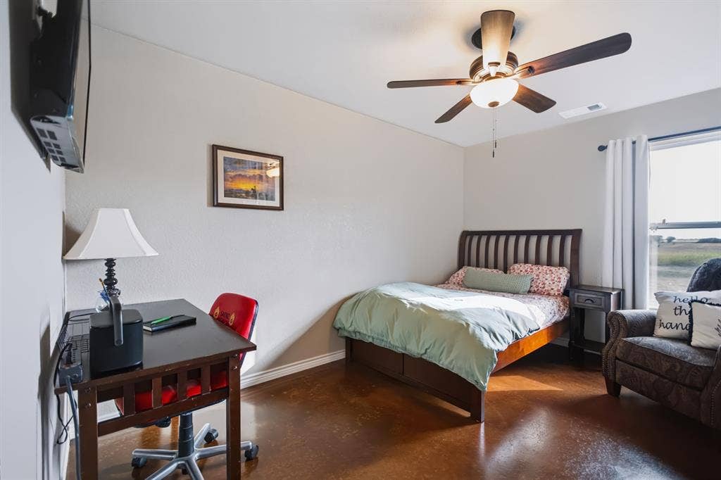 2433 Trlica Road, West, TX 76691 Guest Room 2Smooth finished flooring, wall-mounted television, ceiling fan with integrated lighting, wood-frame bed with slatted headboard, and window with curtains