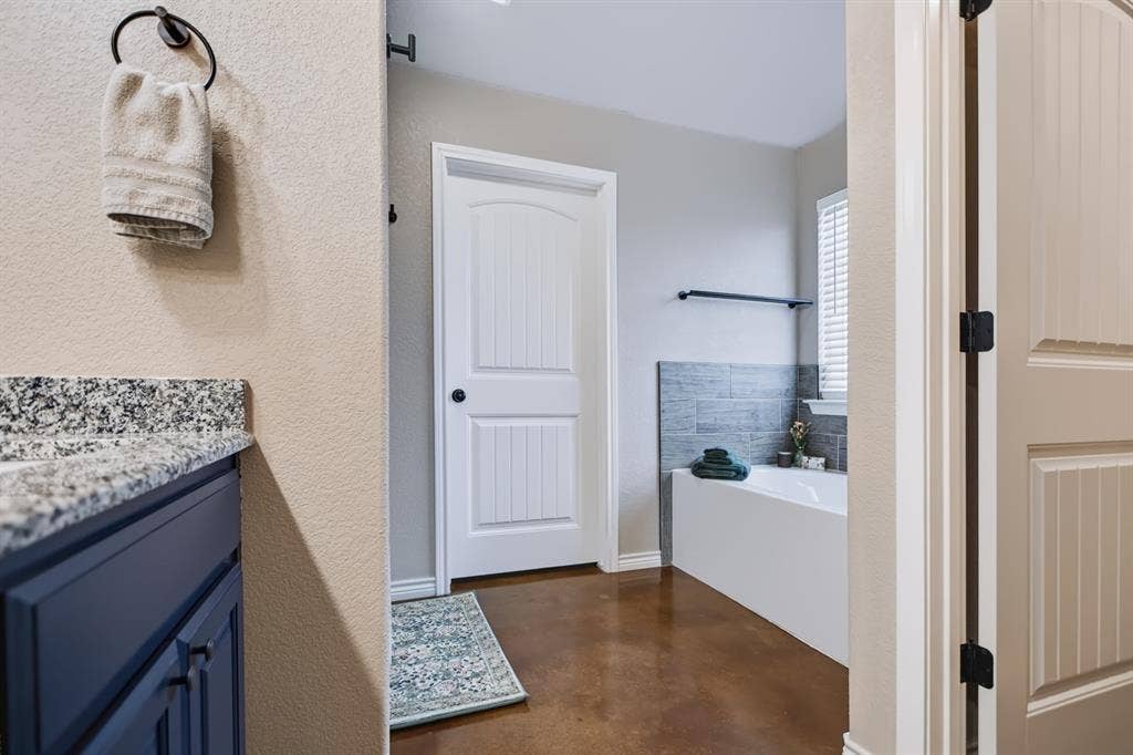 2433 Trlica Road, West, TX 76691 Granite-style countertop, cabinetry with dark finish, wood-finish flooring, built-in tub, and tiled wall accent