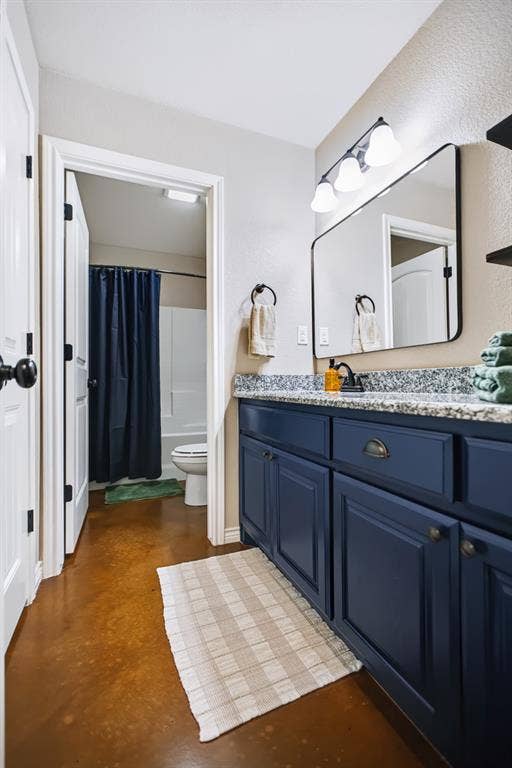 2433 Trlica Road, West, TX 76691 Guest BathroomBathroom featuring a dark blue vanity, speckled countertop, rectangular wall mirror, and dedicated lighting fixture