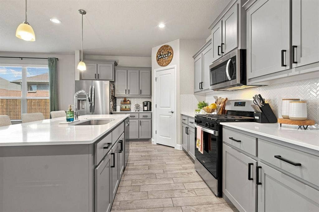 Kitchen featuring gray cabinetry, stainless steel appliances, a large island with an integrated sink, white countertops, and wood-finish flooring