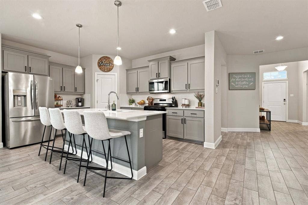 Kitchen featuring stainless steel appliances, an island with seating, pendant lighting, recessed lighting, and wood-finish flooring