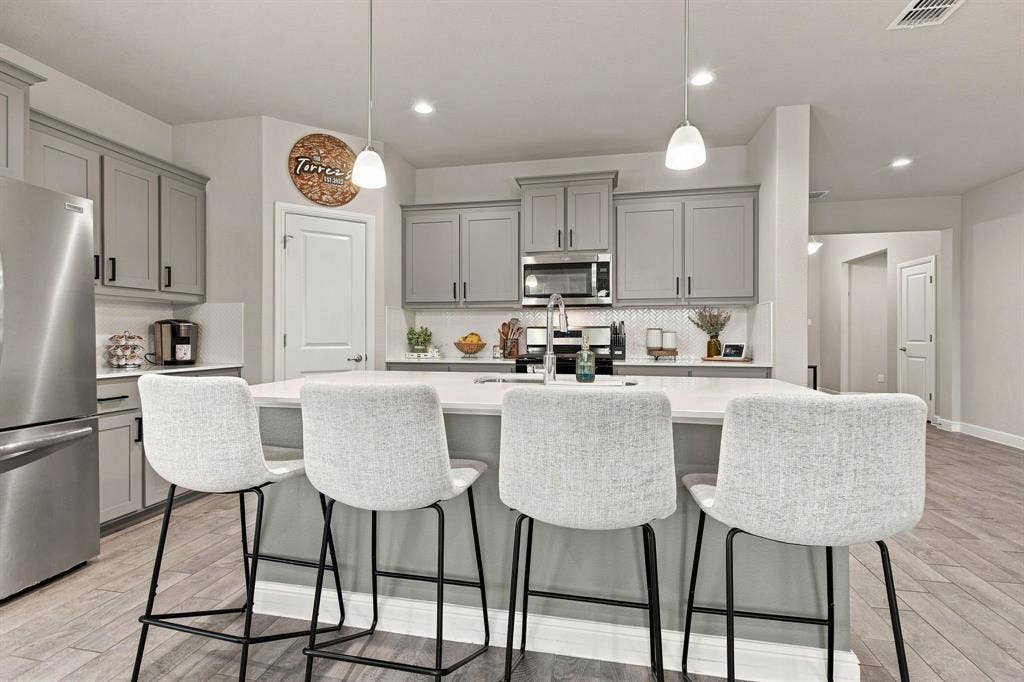 Kitchen featuring a substantial island with seating, stainless steel appliances, grey cabinetry, and wood-finish flooring
