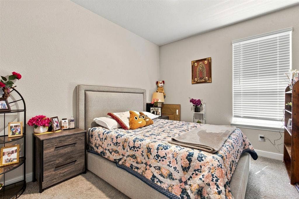 Textured wall finish, upholstered headboard, wood-finish nightstand with drawers, window with blinds, and carpeting