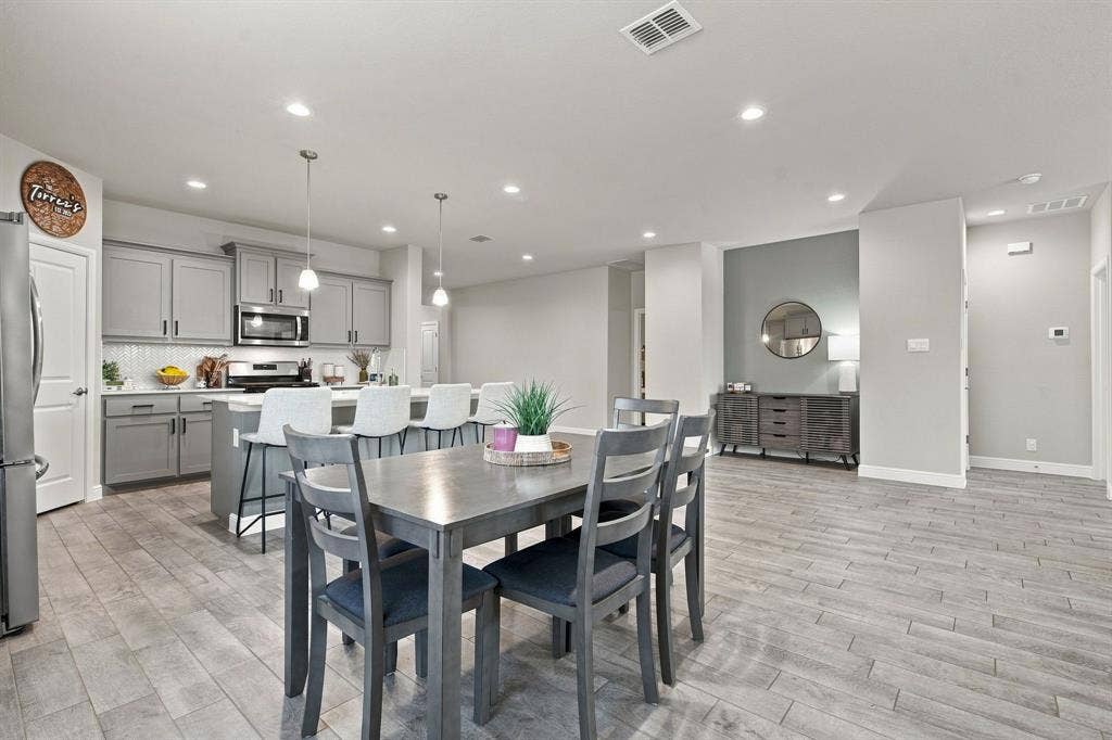 Open-concept living space featuring wood-finish flooring, recessed lighting, and a kitchen with light gray cabinetry, a white tile backsplash, and a central island