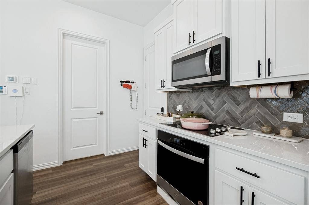 7536 Laburnam Road, Dallas, TX 75228 Kitchen featuring white cabinetry, stainless steel microwave, black electric cooktop, light-toned countertops, and a herringbone pattern tile backsplash