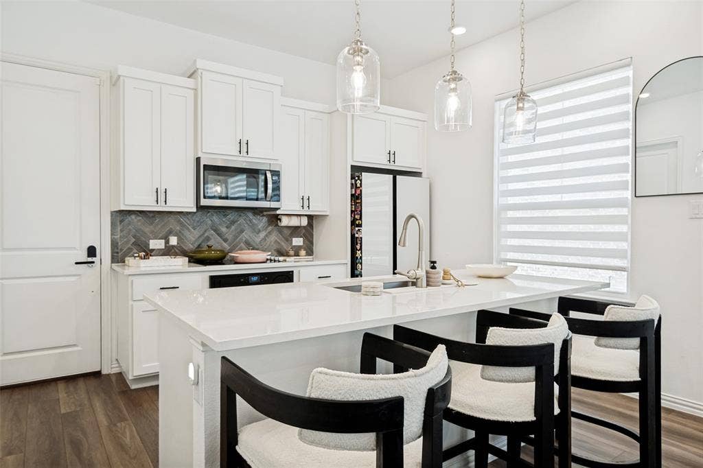 7536 Laburnam Road, Dallas, TX 75228 Kitchen featuring white cabinetry, stainless steel appliances, a white island with an undermount sink, a gray herringbone tile backsplash, and wood-finish flooring