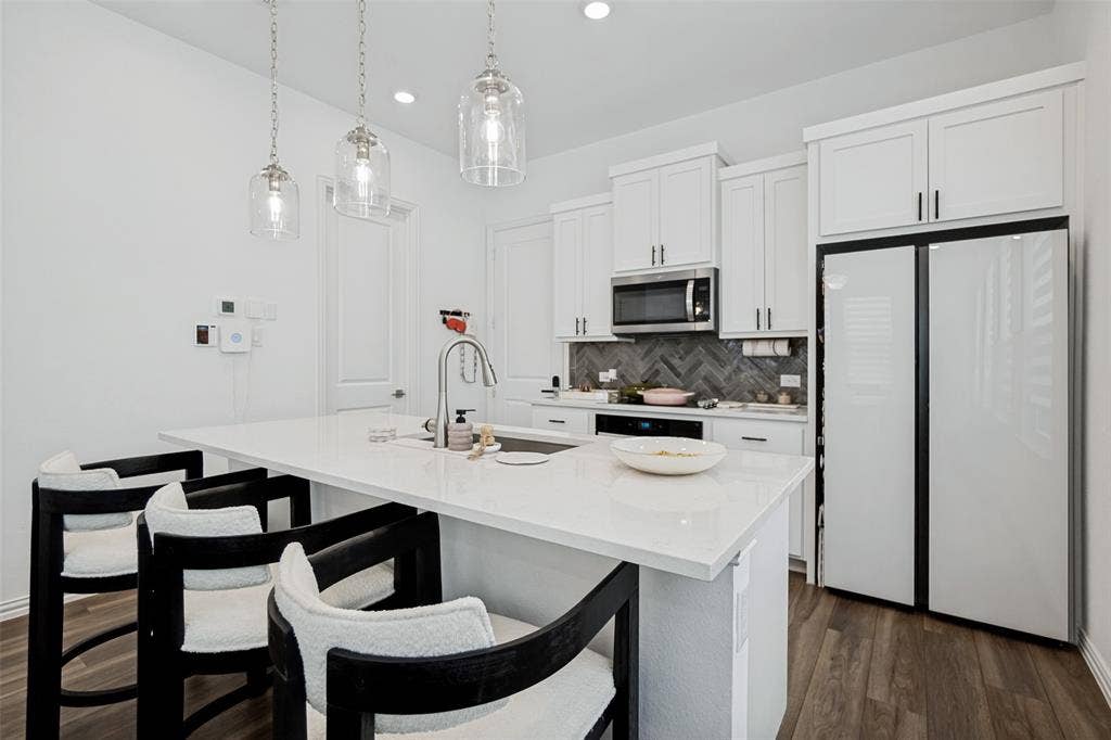 7536 Laburnam Road, Dallas, TX 75228 Kitchen featuring an island with a built-in sink, white cabinetry, a herringbone tile backsplash, stainless steel appliances, and wood-finish flooring