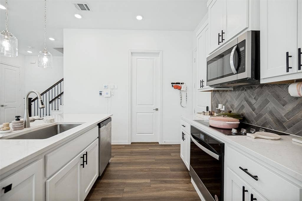 7536 Laburnam Road, Dallas, TX 75228 White cabinetry with black hardware, stainless steel appliances, wood-finish flooring, herringbone tile backsplash, and recessed lighting
