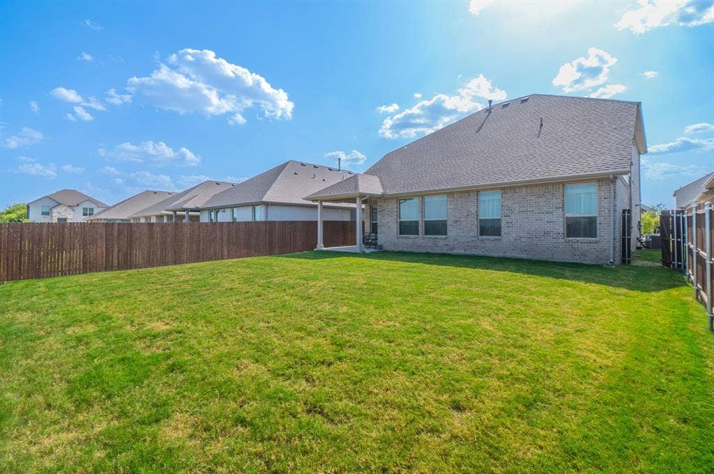 Expansive grassy yard with a privacy fence, covered patio, and brick exterior