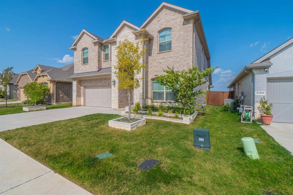 Stone and brick exterior with arched windows, attached garage, concrete driveway, and established landscaping