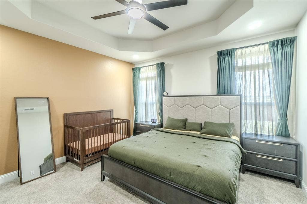 Tray ceiling with a ceiling fan, two windows, and textured wall-to-wall carpeting
