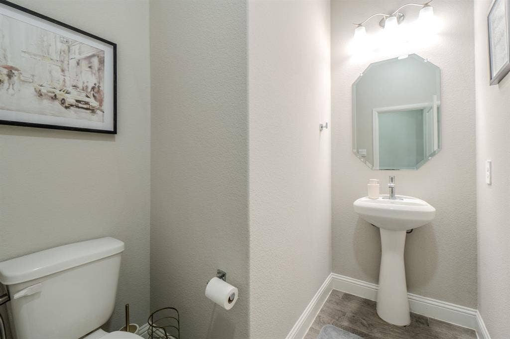 Pedestal sink with a polished chrome faucet, octagonal mirror, and a three-light vanity fixture