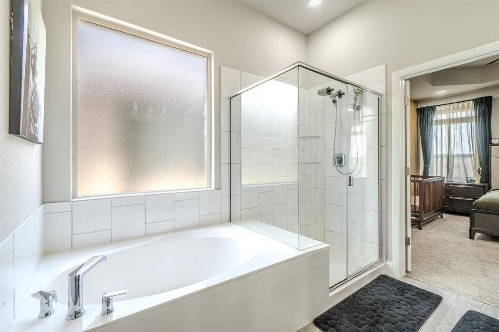 Soaking tub with chrome fixtures, enclosed glass shower, frosted privacy window, and recessed lighting