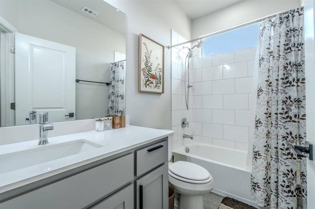 White subway tile shower surround, integrated single basin vanity, gray cabinet vanity with black hardware, chrome faucet, and wood-finish flooring