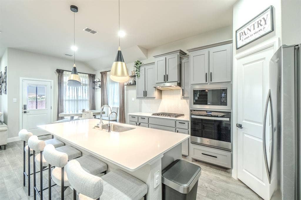 Kitchen featuring a large island with an undermount sink, light gray cabinetry, stainless steel appliances, and wood-finish flooring