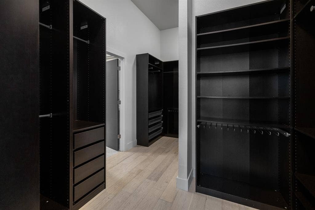 1321 Black Walnut Lane, Arlington, TX 76005 Spacious walk-in closet featuring floor-to-ceiling black cabinetry with multiple shelving sections, integrated drawer storage, and hanging rods for organized wardrobe storage