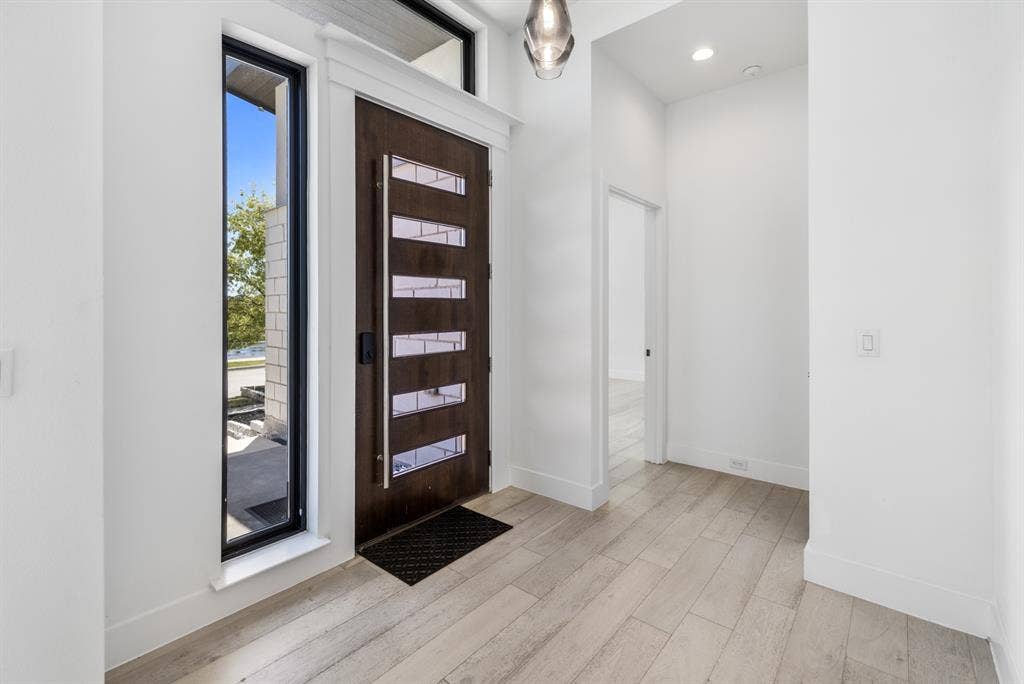 1321 Black Walnut Lane, Arlington, TX 76005 Modern entryway featuring a dark wood contemporary front door with horizontal panel detailing, wide-plank wood-finish flooring, white walls, recessed lighting, and a glass panel entry door with black frame allowing natural light and views of the exterior landscape