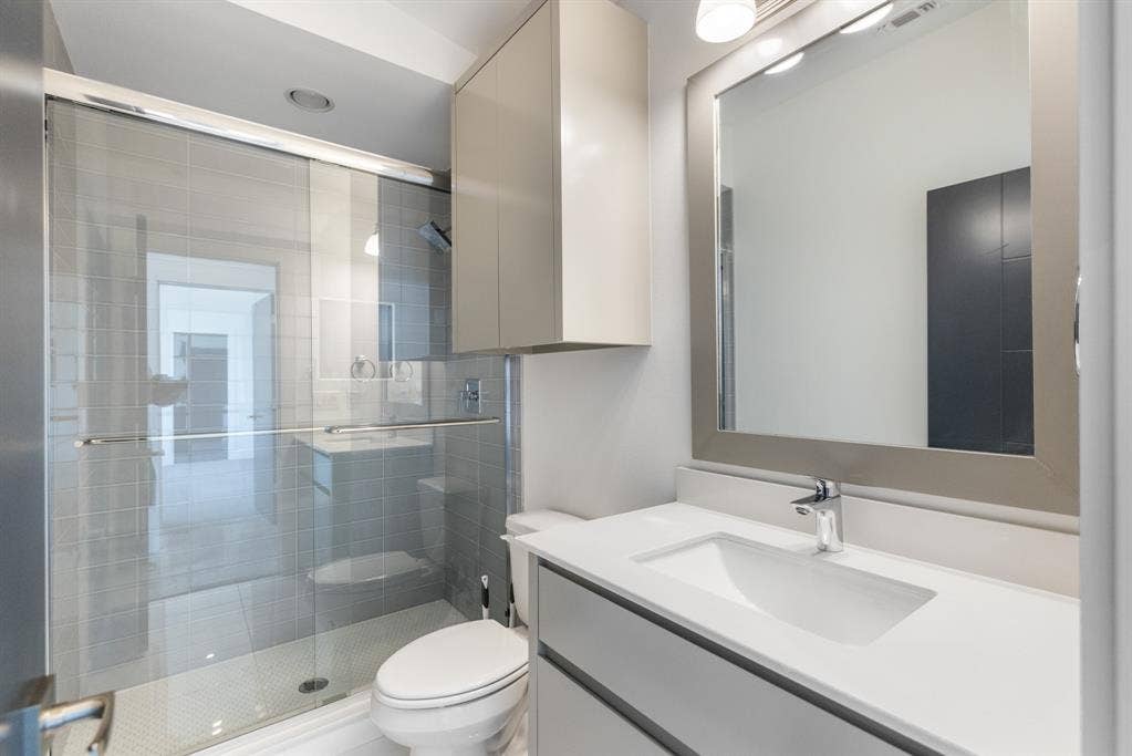 1321 Black Walnut Lane, Arlington, TX 76005 Modern bathroom featuring a frameless glass walk-in shower enclosure with tile surround, a floating vanity with integrated rectangular sink, white quartz countertop, contemporary wall-mounted chrome faucet, and a large framed mirror with integrated lighting