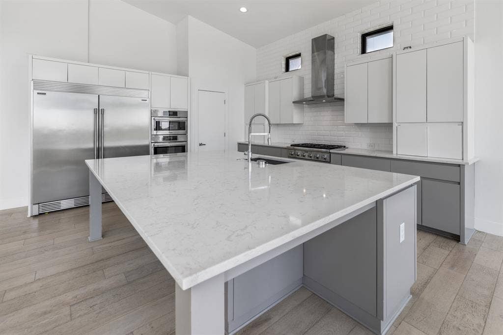1321 Black Walnut Lane, Arlington, TX 76005 Expansive kitchen island with a light-toned countertop, stainless steel appliances, white cabinetry, and wood-finish flooring