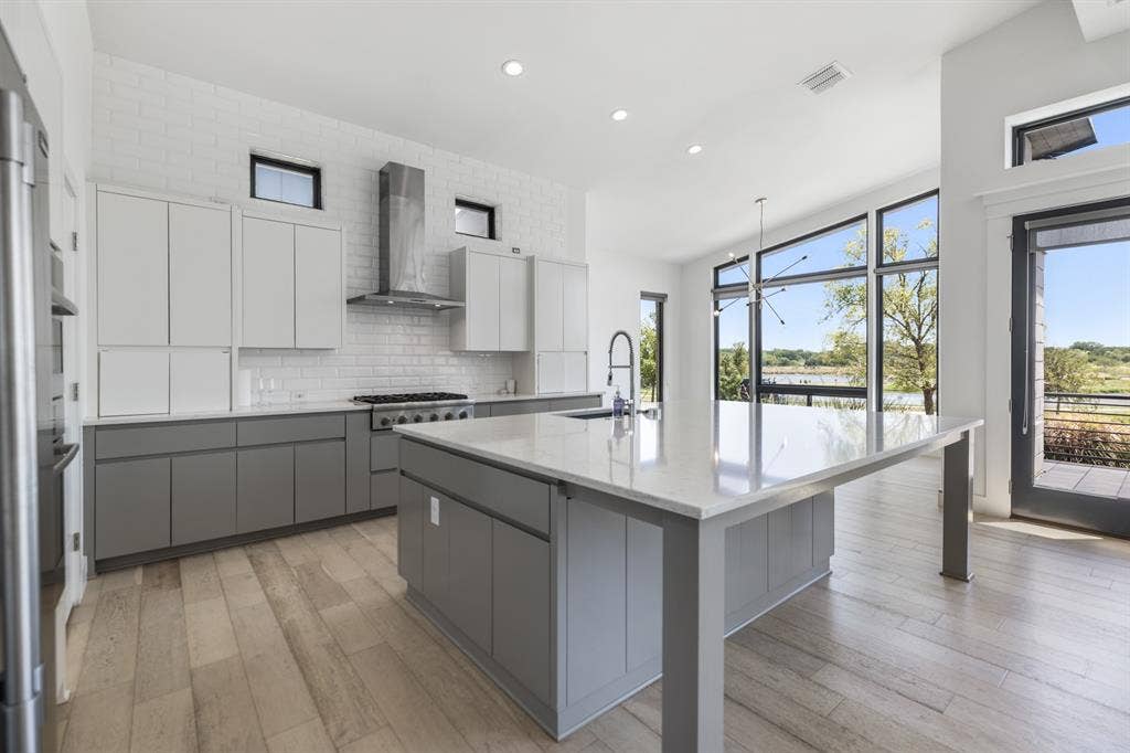1321 Black Walnut Lane, Arlington, TX 76005 Modern kitchen featuring a large central island with a solid surface countertop, two-tone cabinetry, wood-finish flooring, and a stainless steel range hood