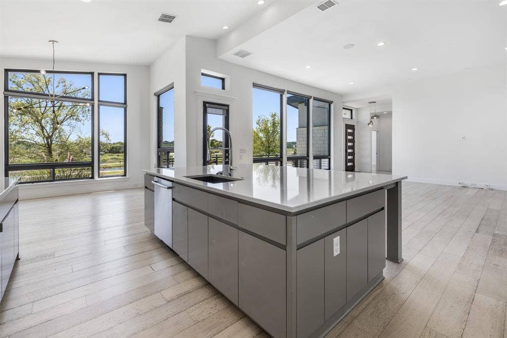1321 Black Walnut Lane, Arlington, TX 76005 Kitchen island featuring a single basin sink, pull-down faucet, integrated dishwasher, and light-toned countertop