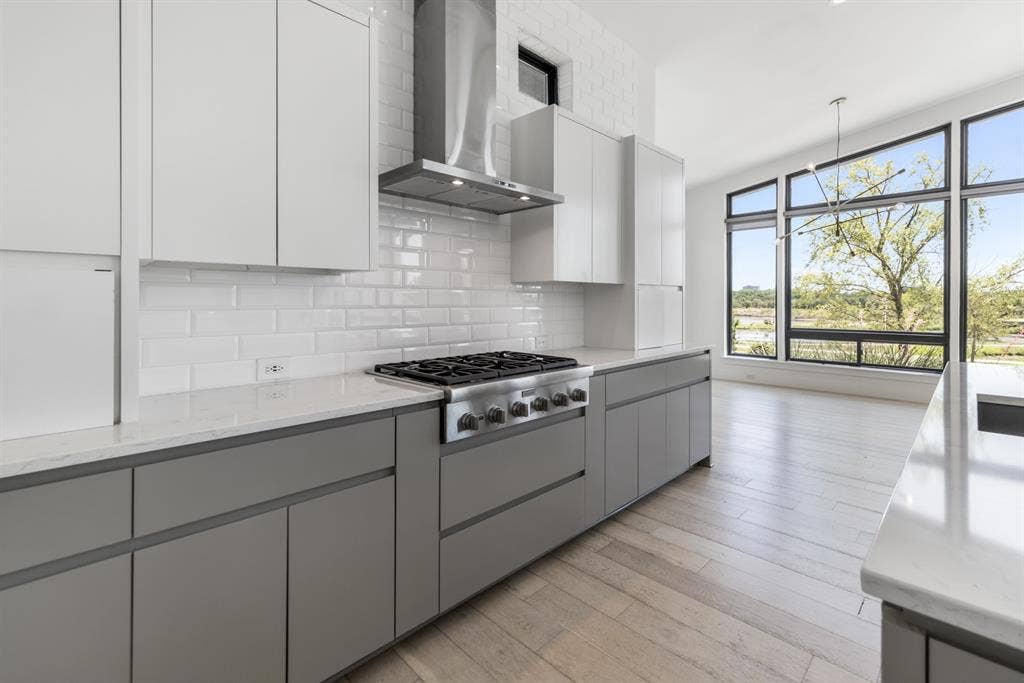 1321 Black Walnut Lane, Arlington, TX 76005 Modern kitchen featuring white cabinetry with gray lower cabinets, stainless steel gas range with overhead hood ventilation, white subway tile backsplash, and wood-finish flooring